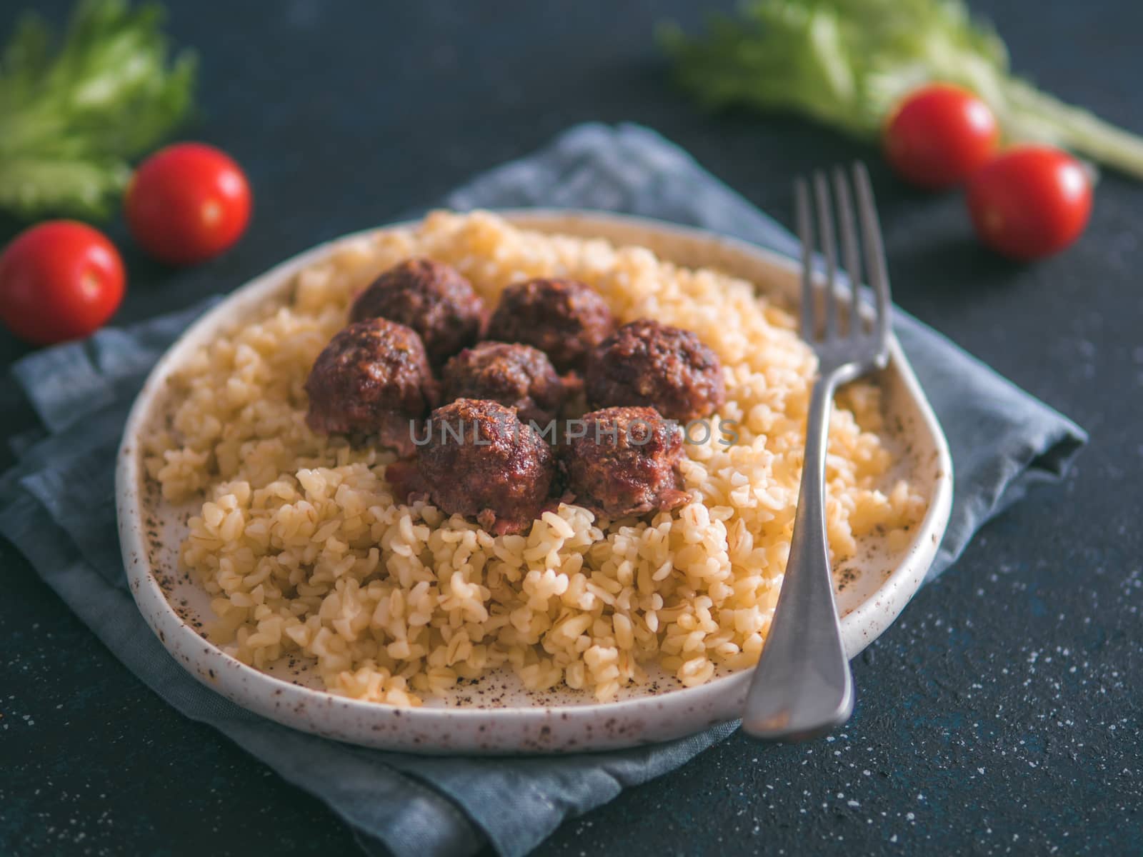 Bulgur dish idea and recipe. Bulgur with homemade roasted beef meatballs on dark blue background. Copy space for text. Shallow DOF