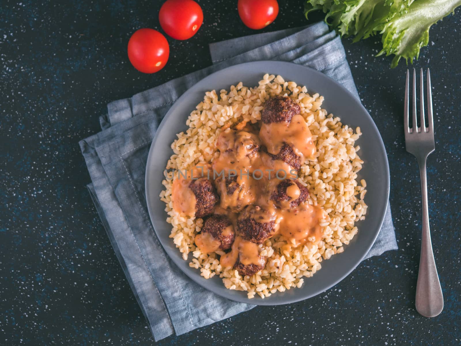 Bulgur dish idea and recipe. Bulgur with homemade roasted beef meatballs on dark blue background. Copy space for text. Top view or flat-lay.