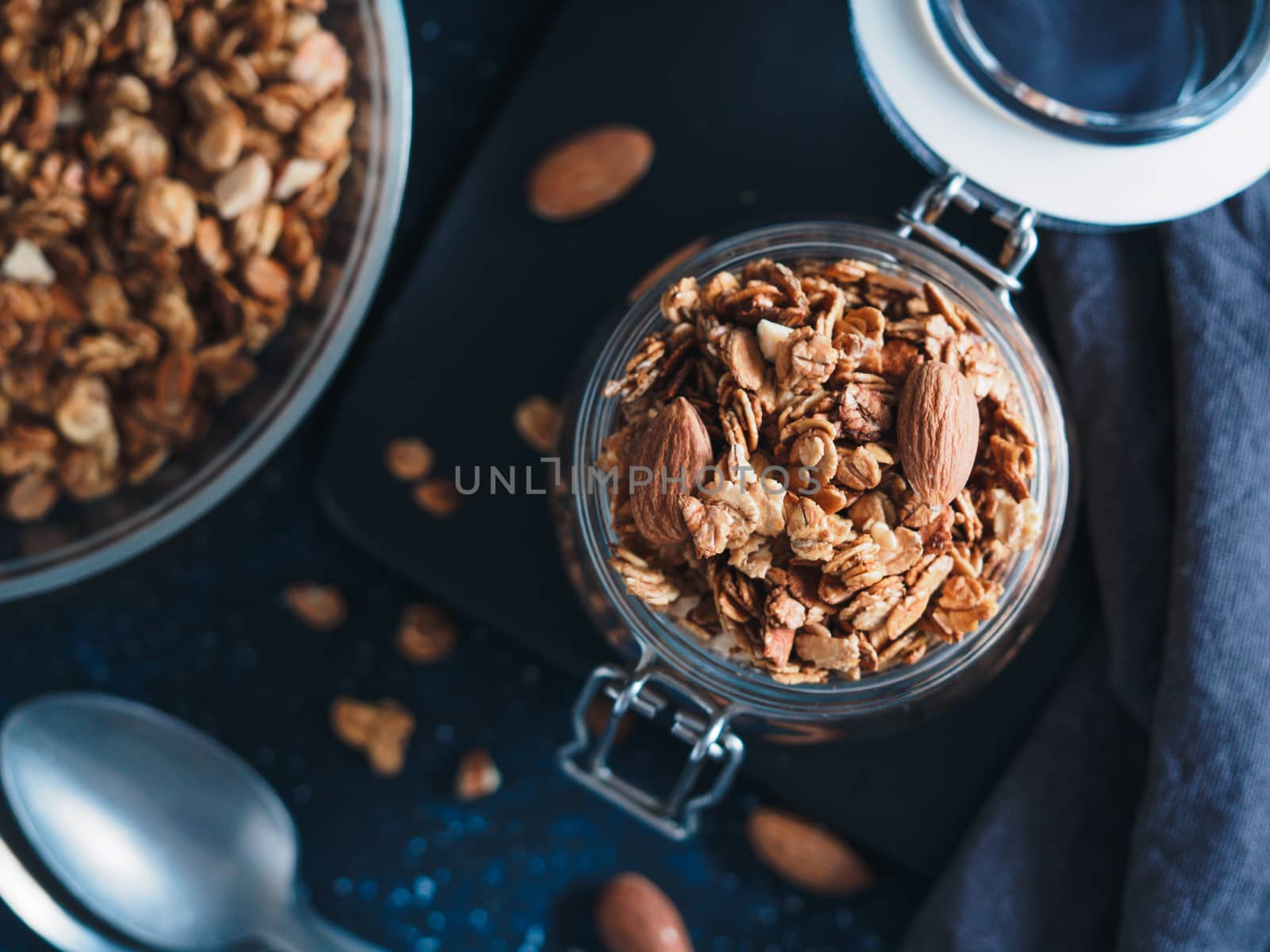 Homemade granola in glass jar on dark table. Ingredients for healthy breakfast. Copy space for text. Low key. Selective focus. Shallow DOF. Top view or flat-lay.