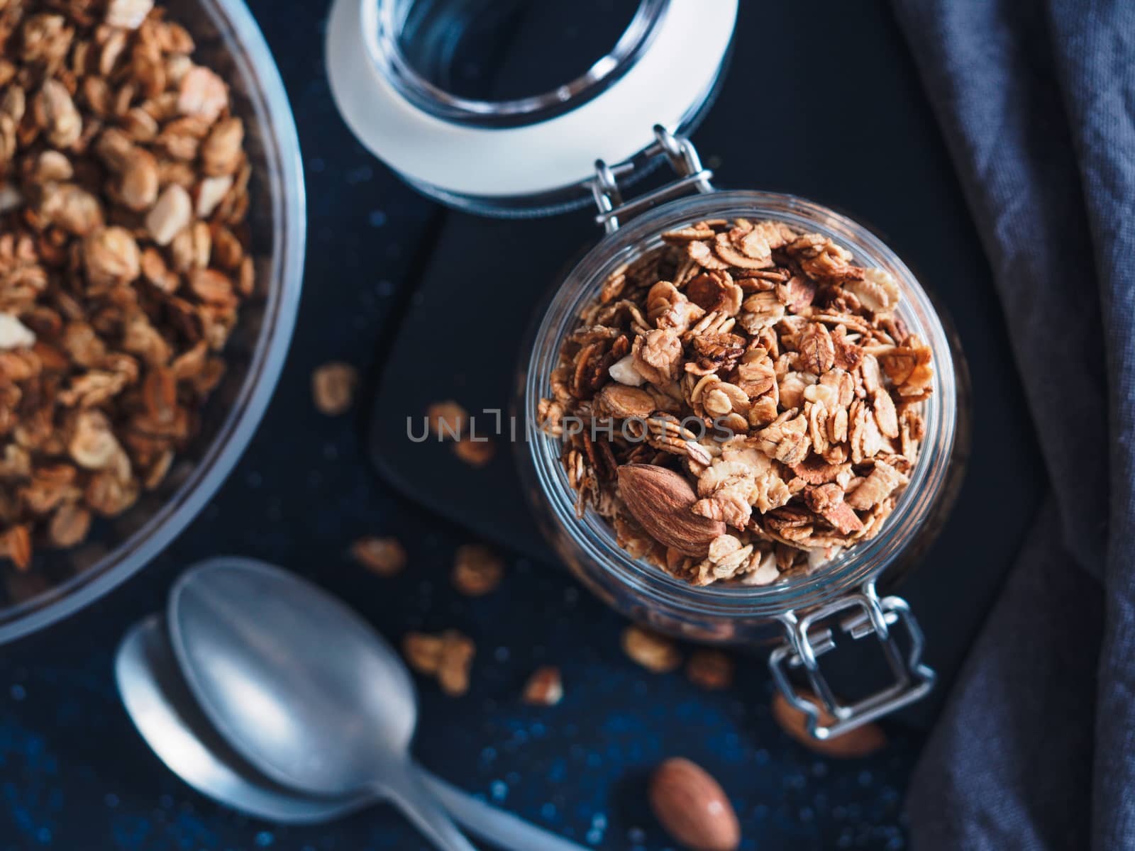 Homemade granola in glass jar on dark table. Ingredients for healthy breakfast. Copy space for text. Low key. Selective focus. Shallow DOF. Top view or flat-lay.