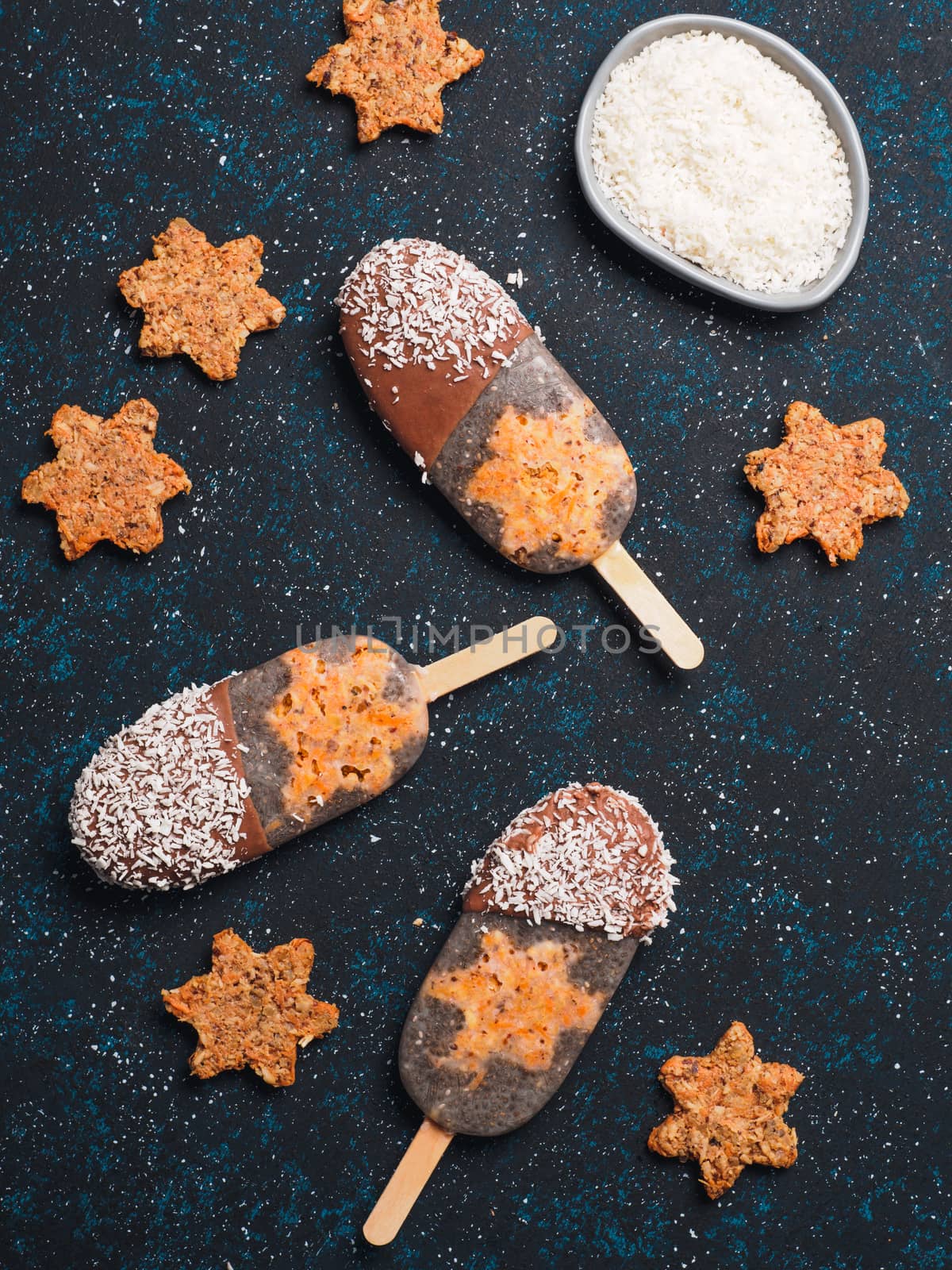 Chia popsicle with raw carrot cake and chocolate on dark blue background. Healthy recipe and idea homemade vegan popsicle ice cream. Easter dessert idea. Top view or flat-lay. Vertical.