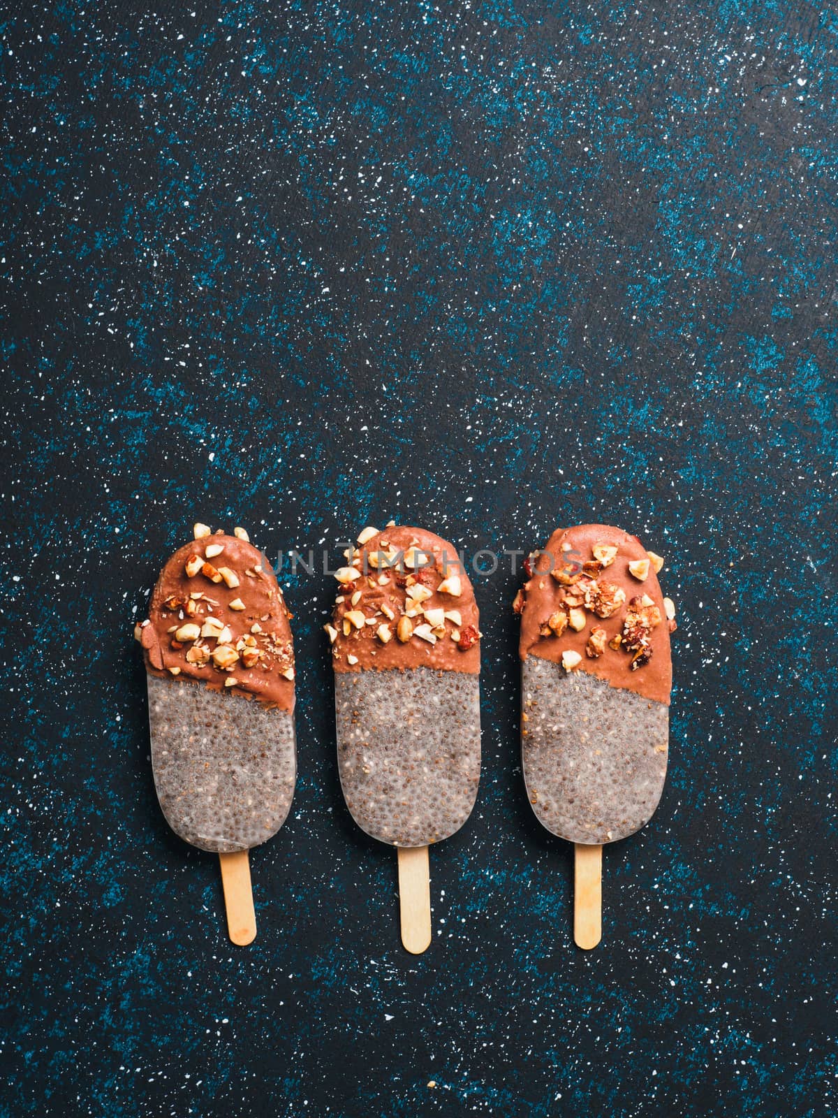 Chia popsicle with chocolate and nuts on blue background. Healthy recipe and idea homemade vegan popsicle ice cream. Easter dessert idea. Copy space for text. Top view or flat-lay. Vertical.