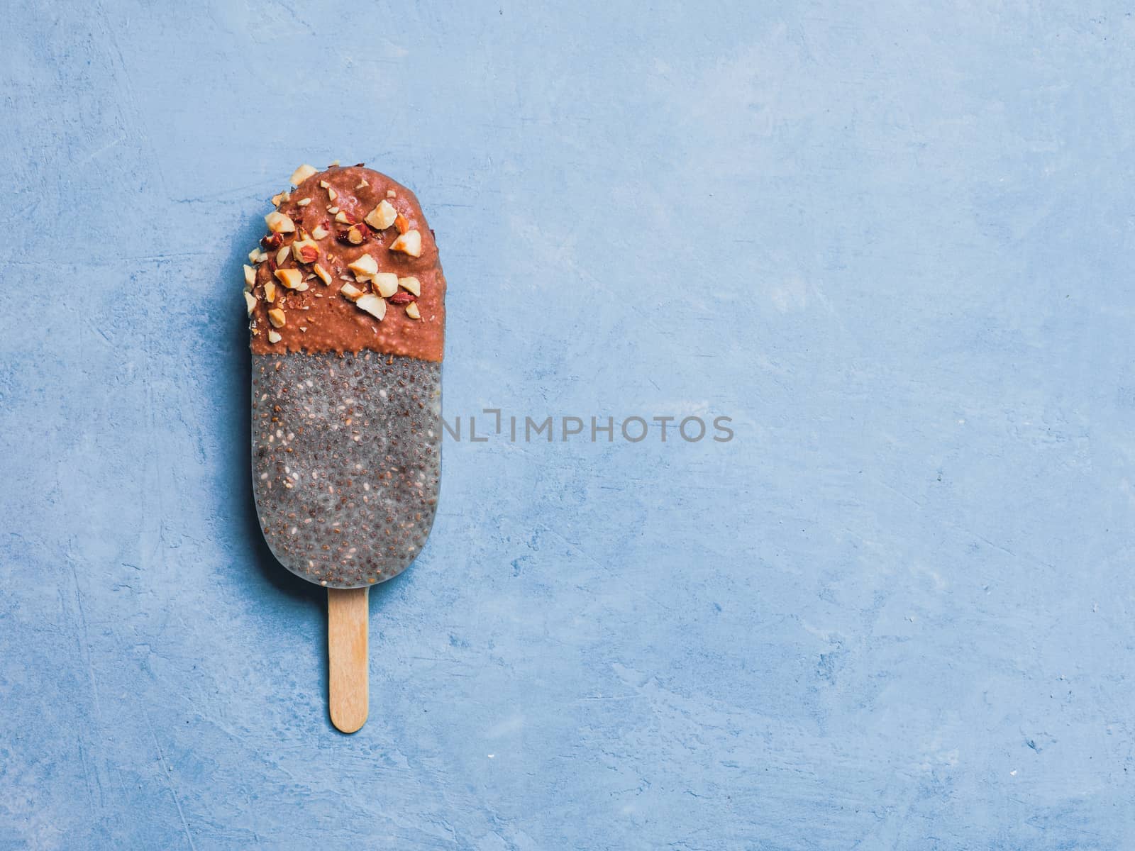 Chia popsicle with chocolate and nuts on blue background. Healthy recipe and idea homemade vegan popsicle ice cream. Easter dessert idea. Copy space for text. Top view or flat-lay.