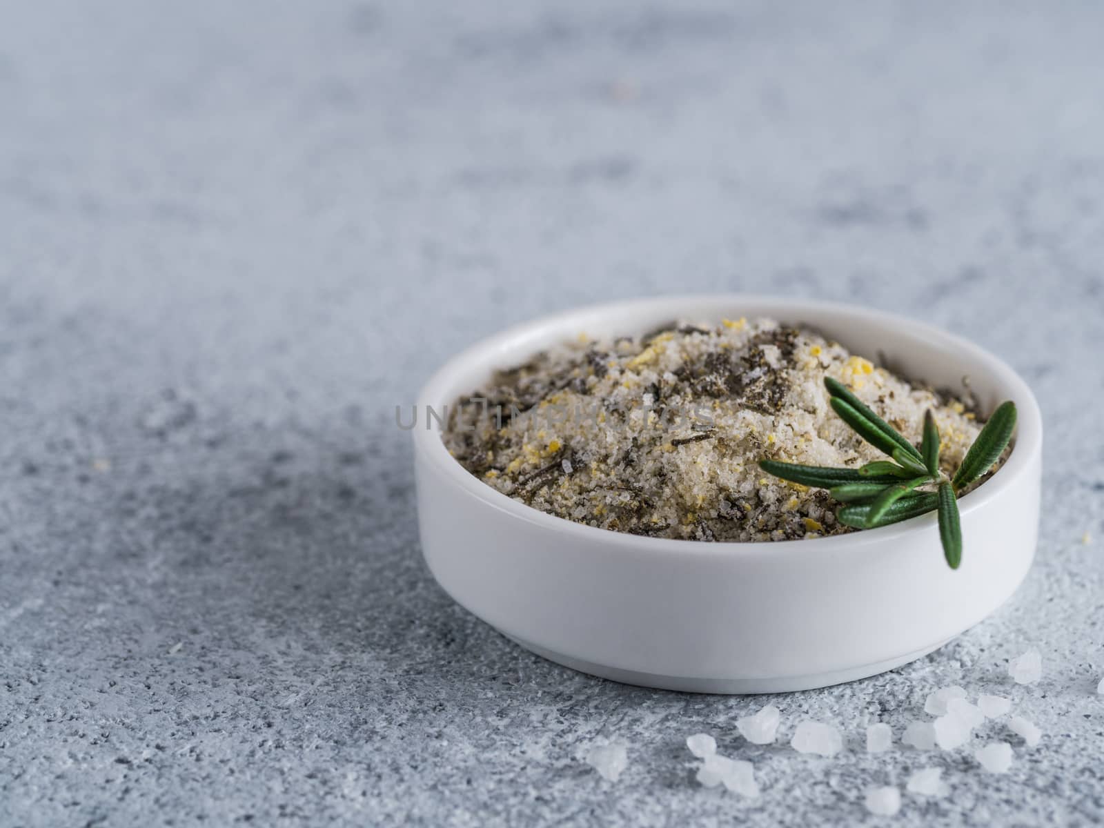 Sea salt scented herb rosemary and lemon zest. Sea salt with aromatic herbin small bowl on gray cement background. Scented salt and ingerdients. Copy space