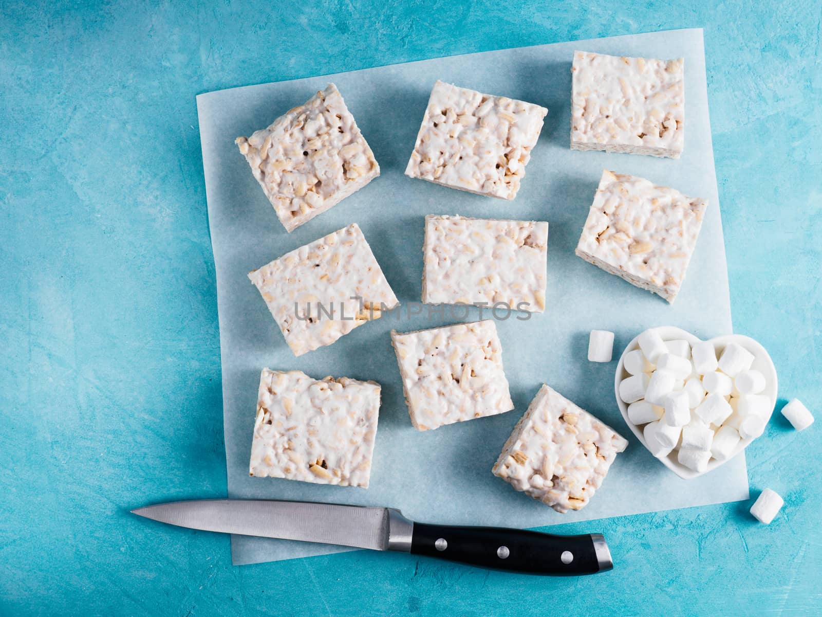 Homemade square bars of Marshmallow and crispy rice and ingredients on blue background. American dessert with marshmallow and crispy rice. Top view. Copy space