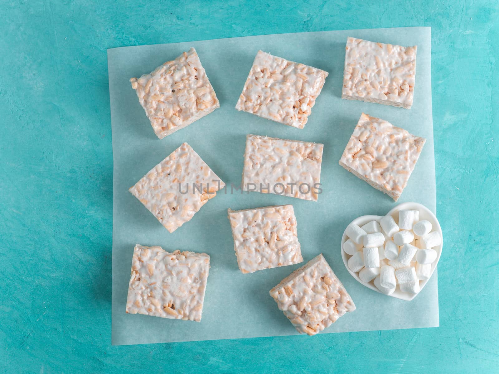 Homemade square bars of Marshmallow and crispy rice and ingredients on azure blue background. American dessert with marshmallow and crispy rice. Top view. Copy space