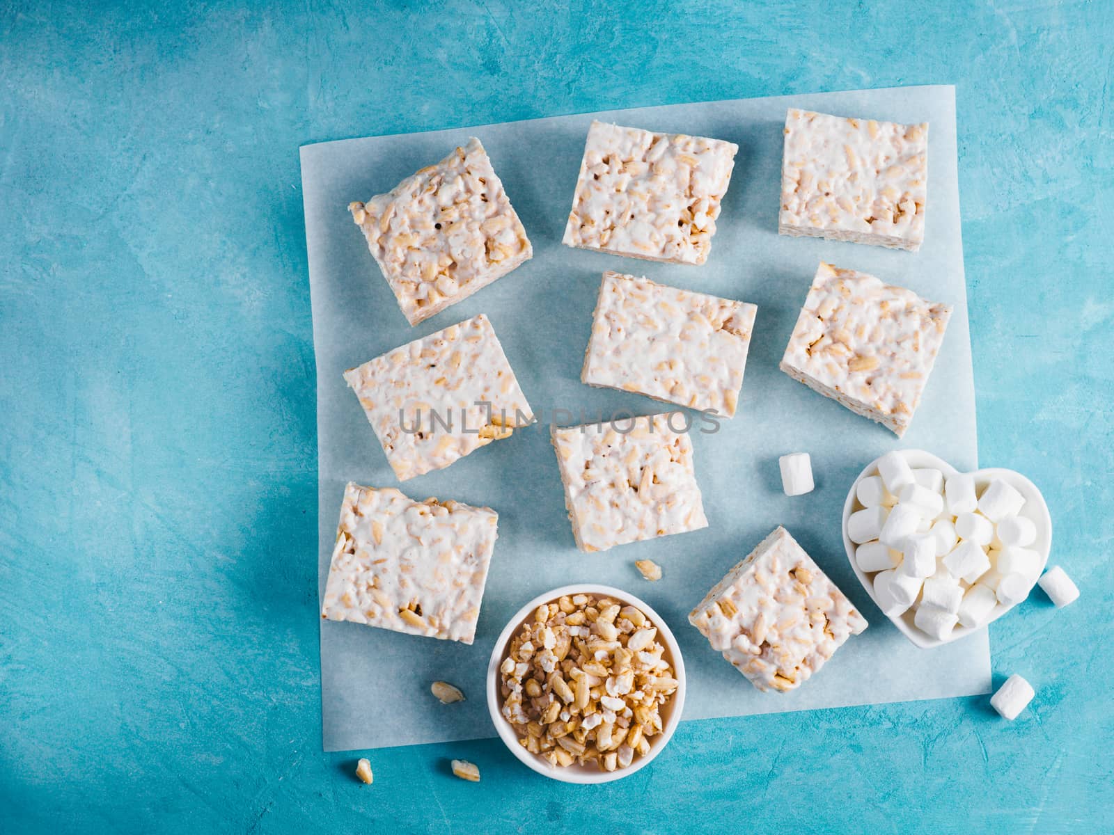 Homemade square bars of Marshmallow and crispy rice and ingredients on blue background. American dessert with marshmallow and crispy rice. Top view. Copy space