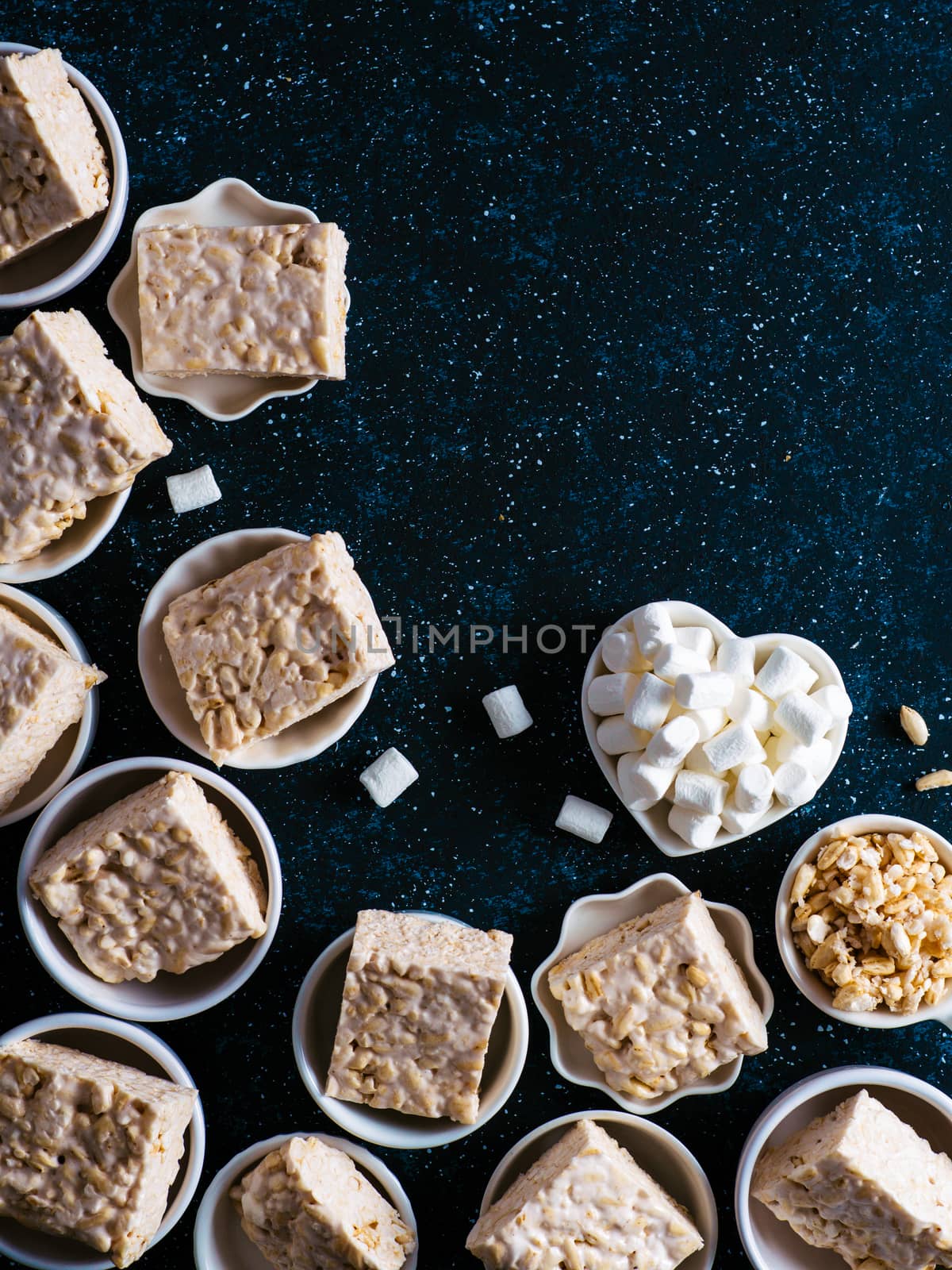 Homemade square bars of Marshmallow and crispy rice and ingredients on dark blue background. American dessert with marshmallow and crispy rice. Top view. Copy space