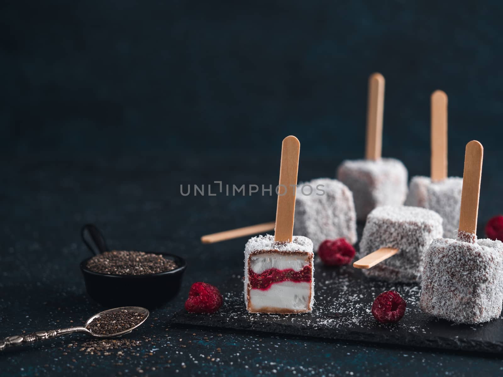 Homemade raw lamington ice cream pops on dark background. Australian sweet dessert lamington with chia and raspberries jam, chocolate and cocoa coat. Vegan food recipe and idea. Copy space for text