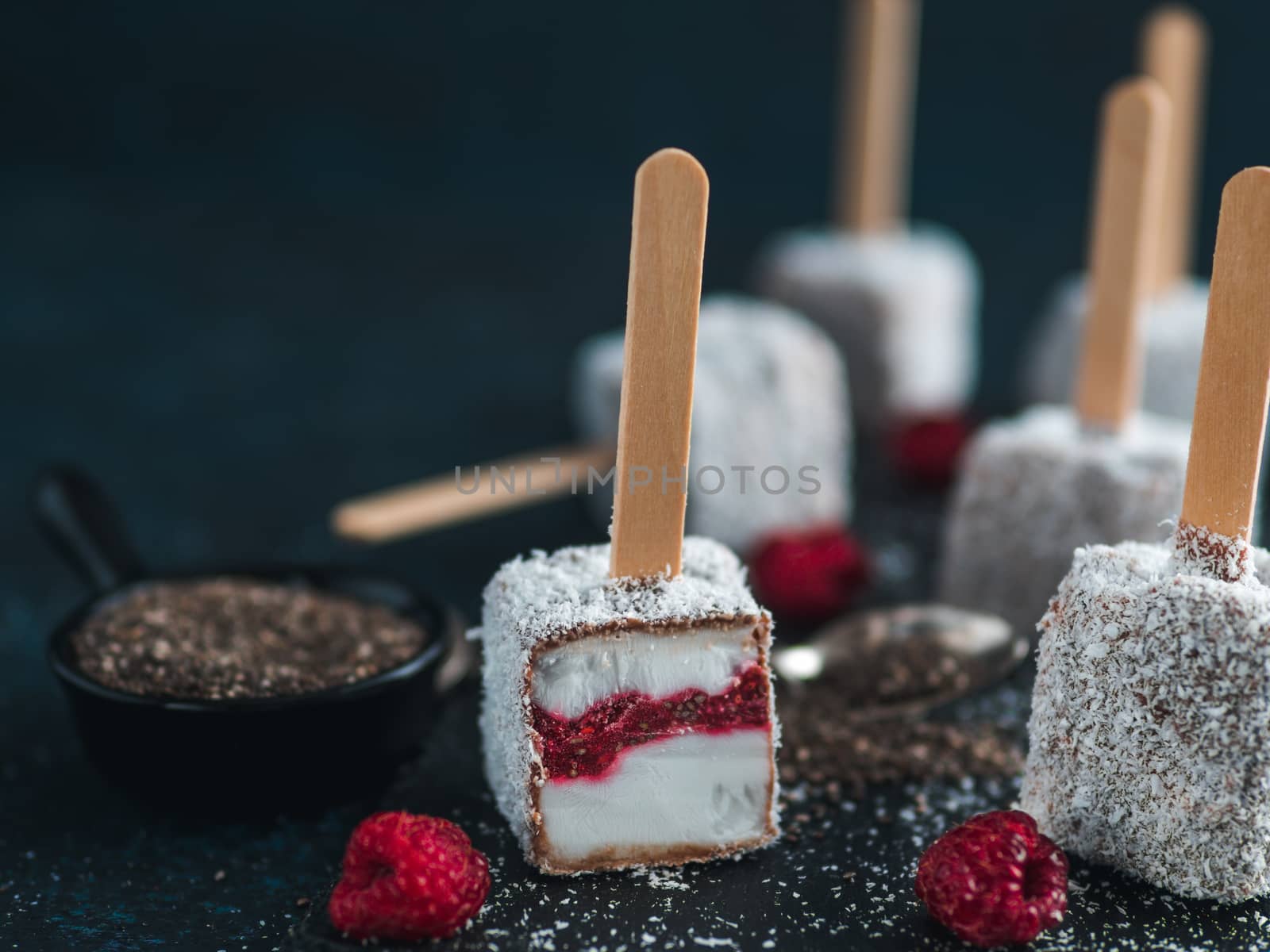 Homemade raw lamington ice cream pops on dark background. Australian sweet dessert lamington with chia and raspberries jam, chocolate and cocoa coat. Vegan food recipe and idea. Copy space for text