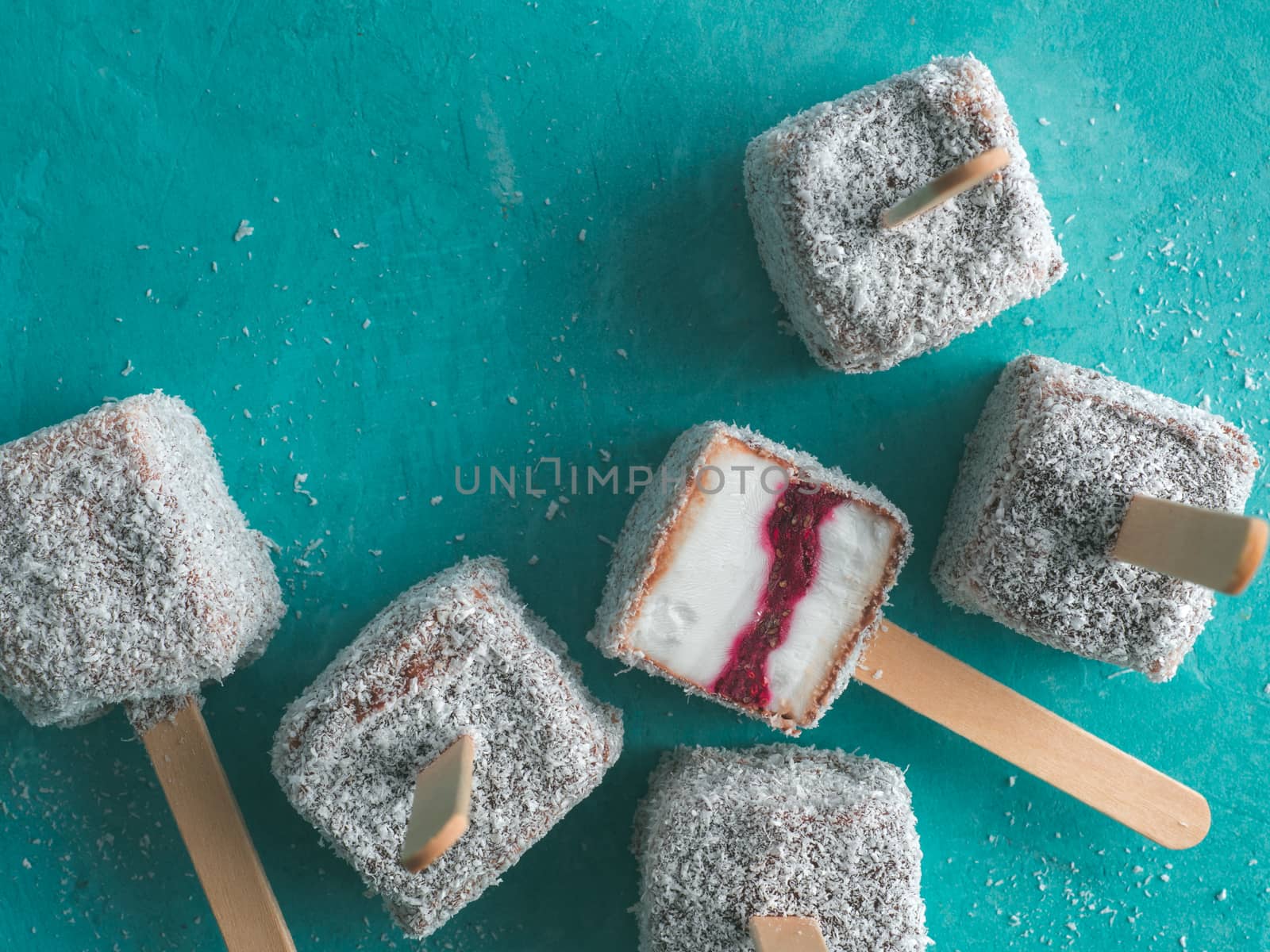 Homemade raw lamington ice cream pops on blue background. Australian sweet dessert lamington with chia and raspberries jam, chocolate and cocoa coat. Vegan food recipe and idea. Top view or flat-lay.