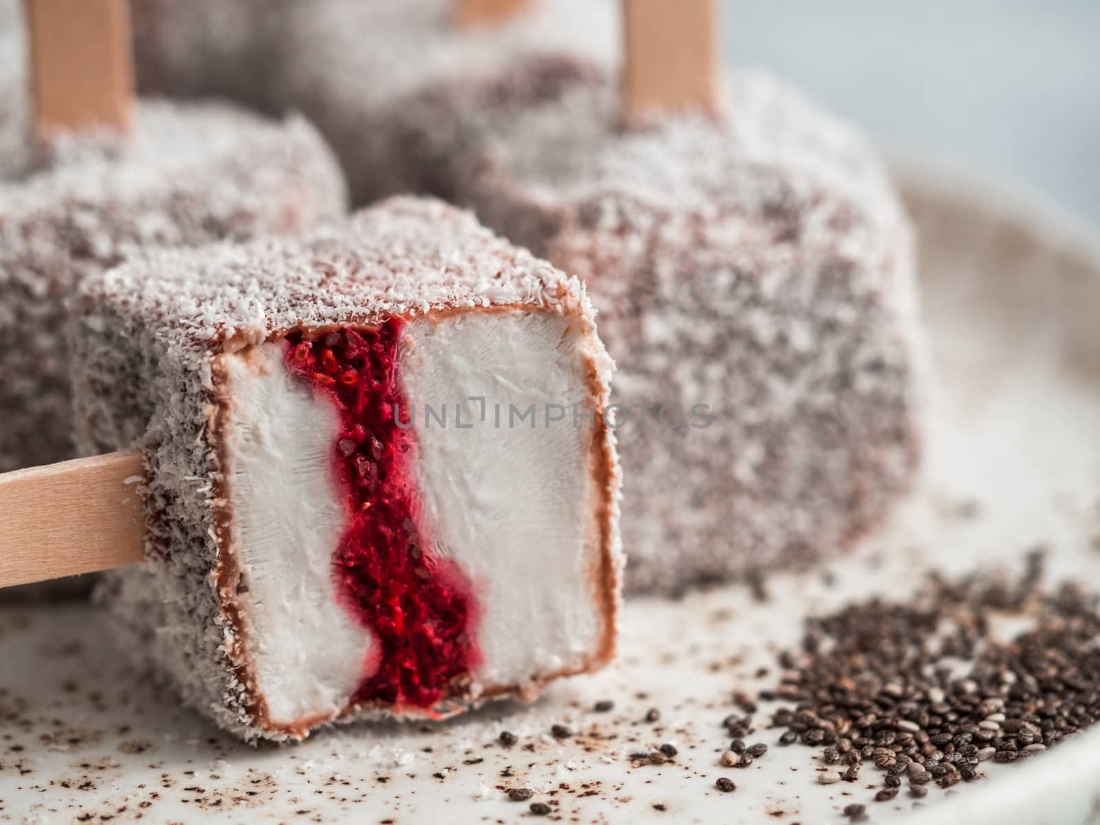 Homemade raw lamington ice cream pops on light background. Australian sweet dessert lamington with chia and raspberries jam, chocolate and cocoa coat. Vegan food recipe and idea. Copy space. Close up