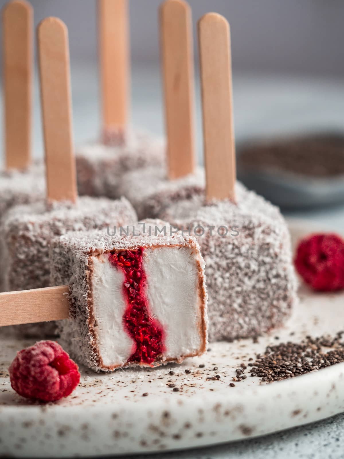 Homemade raw lamington ice cream pops on light background. Australian sweet dessert lamington with chia and raspberries jam, chocolate and cocoa coat. Vegan food recipe and idea. Copy space. Close up