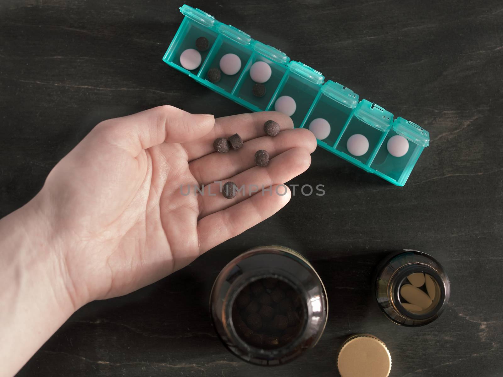Hand with pills and pillbox. Top view of seven day pill box with pills. Green pill-box over dark wooden table. Open pill box and open boxes with pills or vitamins. Copy space. Top view or flat-lay.