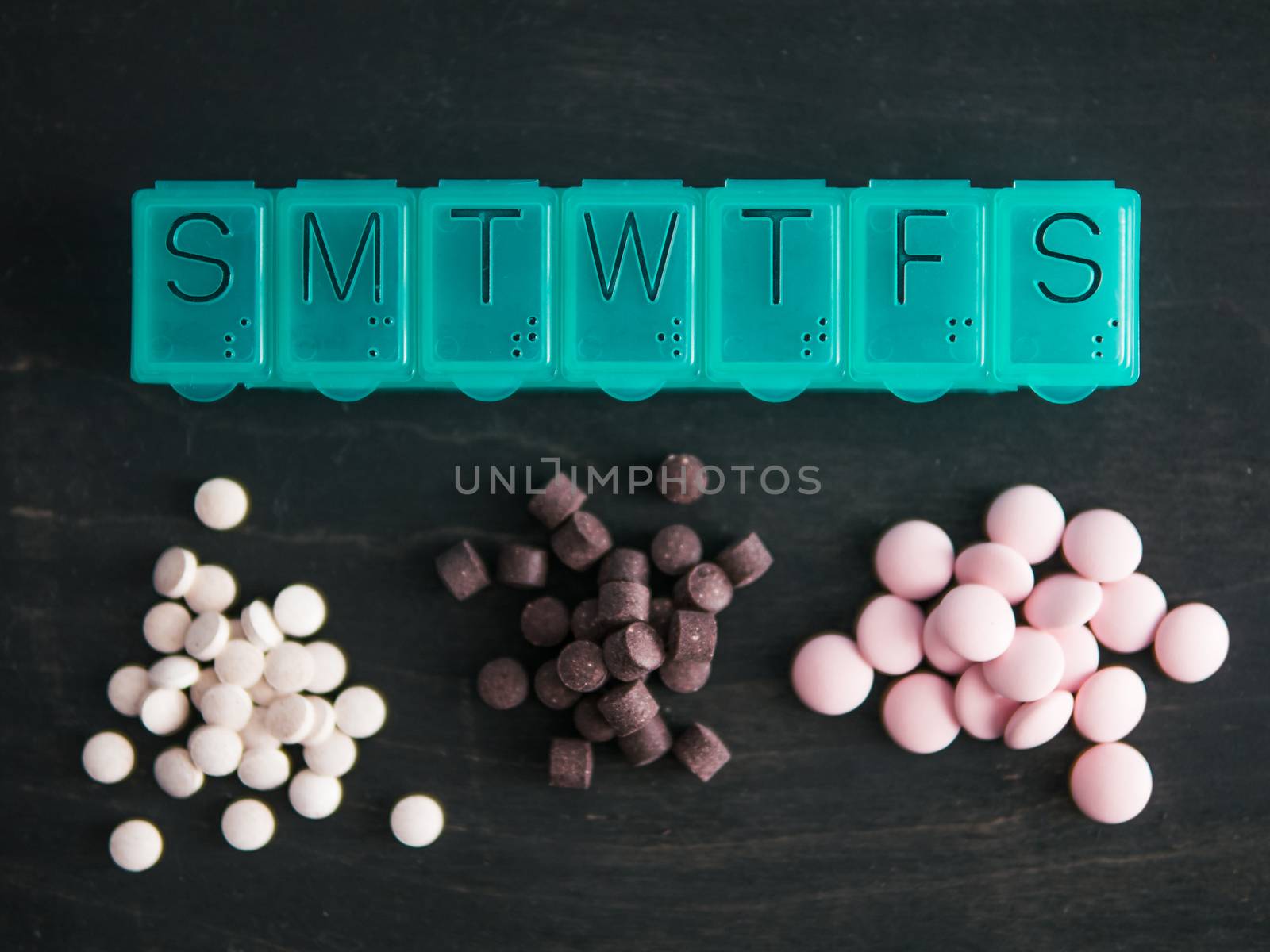 Top view of seven day pill box and heap of pills. Green pill-box over dark wooden table. Pill box and heaps pills or vitamins. Top view or flat-lay.