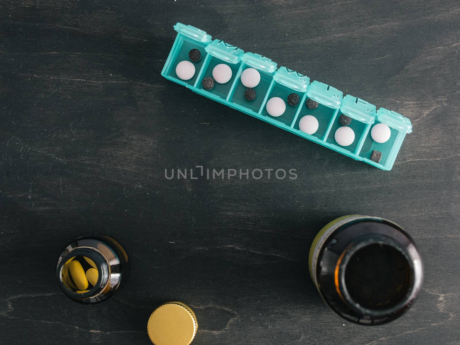 Top view of seven day pill box with pills. Green pill-box with pills visible. Open pill box and jars on dark wooden table. Copy space. Top view or flat lay.Healthy lifestyle and medical concept