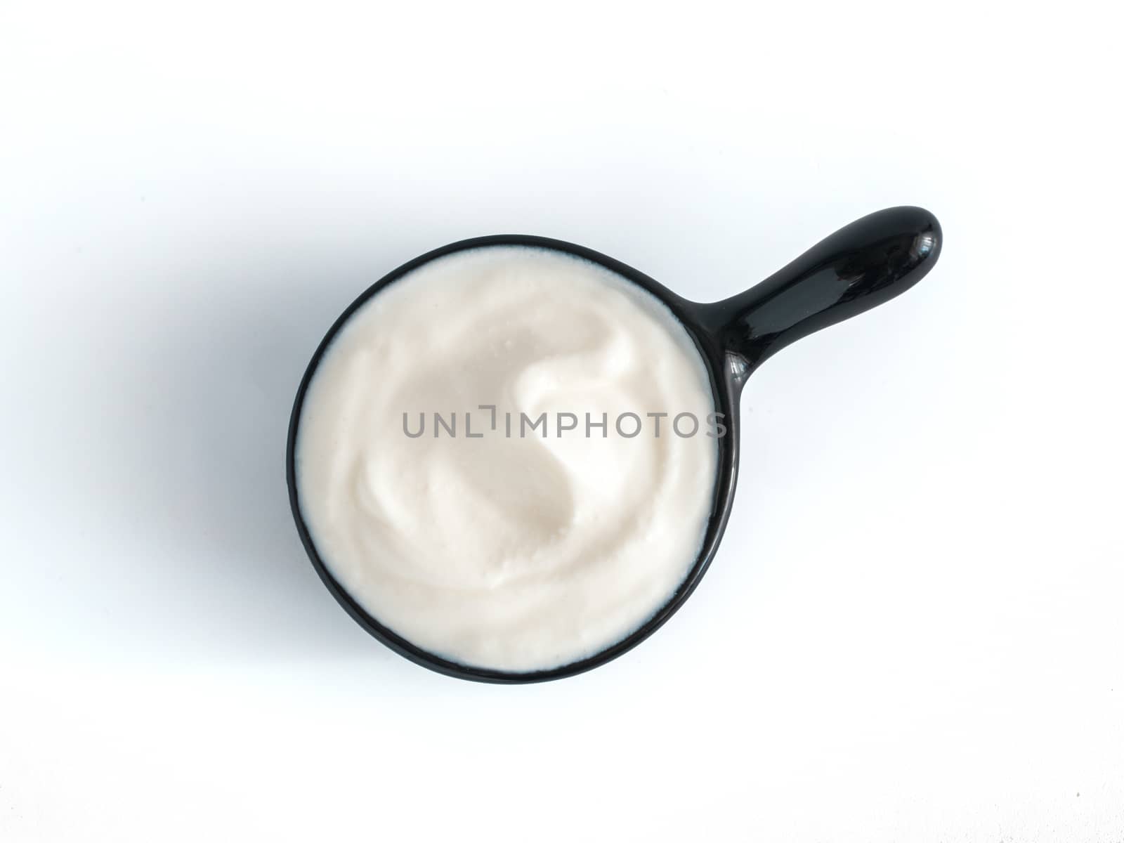 Beautiful greek yogurt or sour cream in black bowl, isolated on white background with clipping path. Top view or flat-lay.