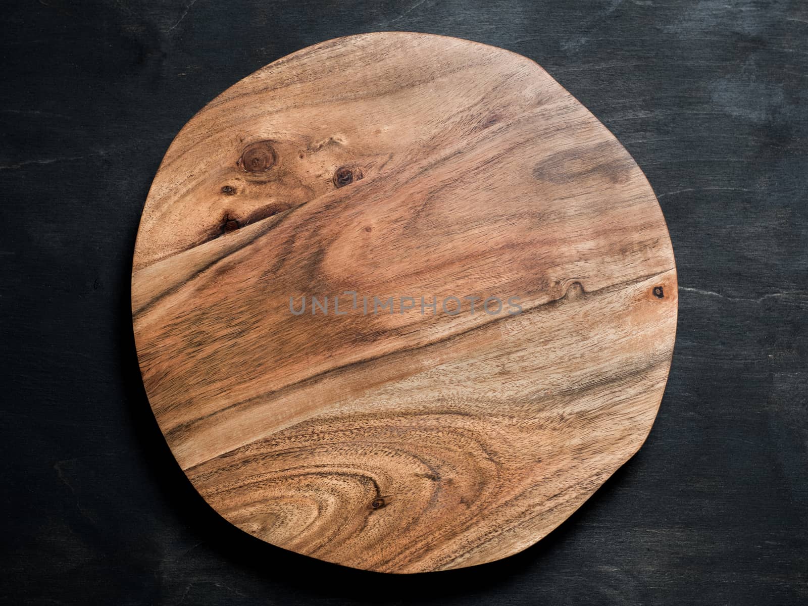Round wooden tray or cutting board on black table. Top view of empty kitchen trendy rustic wooden tray saw cut imitation on black wooden background. Copy space for text. Food and menu background.