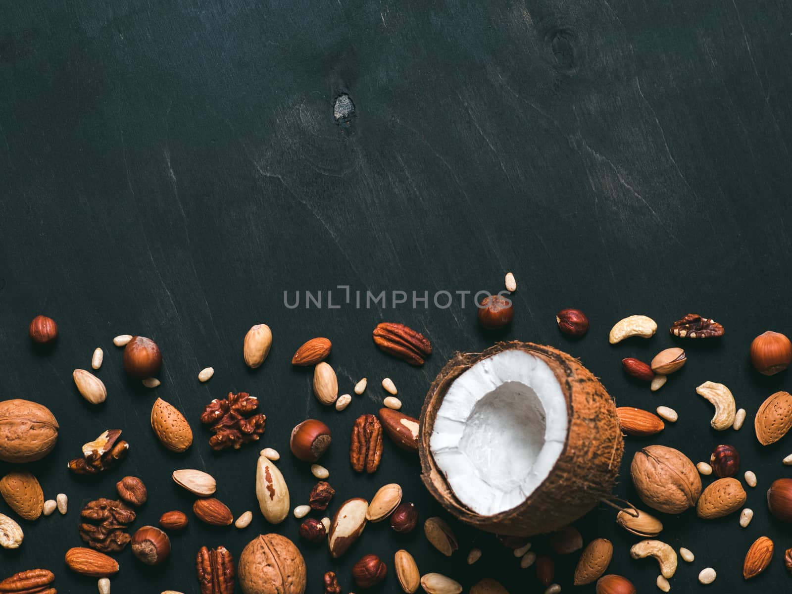 Background of mixed nuts - coconut, hazelnuts, walnuts, almonds, pecan, pistachio, brazil nut, pine nuts, peanut - on dark background. Copy space. Isolated one edge. Top view or flat lay
