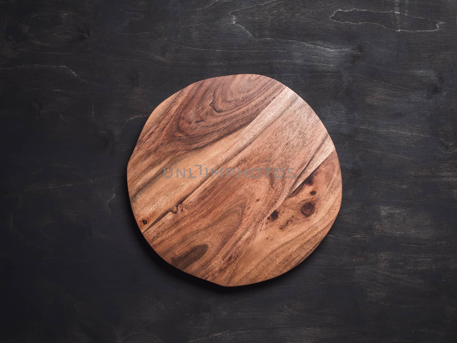 Round wooden tray or cutting board on black table. Top view of empty kitchen trendy rustic wooden tray saw cut imitation on black wooden background. Copy space for text. Food and menu background.