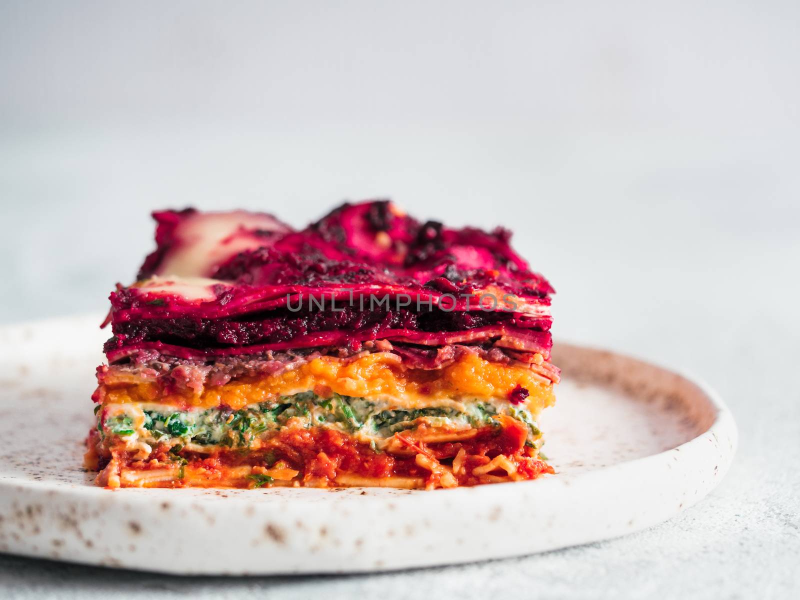 Vegetable Packed Rainbow Lasagne on craft plate. Ideas and recipes for healthy vegetarian dinner or lunch. Lasagne with beetroot, pumpkin, mushrooms, ricotta, spinach, mozarella. Copy space for text.