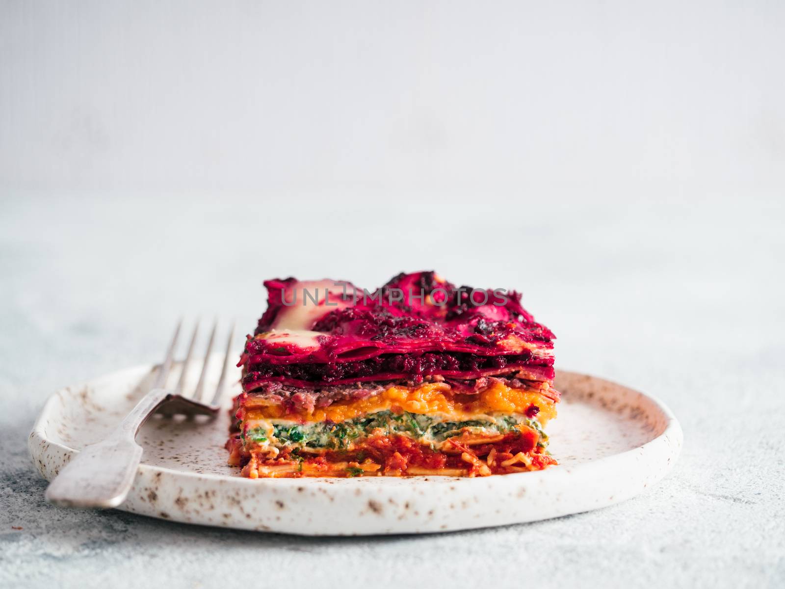 Vegetable Packed Rainbow Lasagne on craft plate.Ideas and recipes for healthy vegetarian dinner or lunch. Lasagne with beetroot,pumpkin,mushrooms,ricotta,spinach,mozarella on white table. Copy space