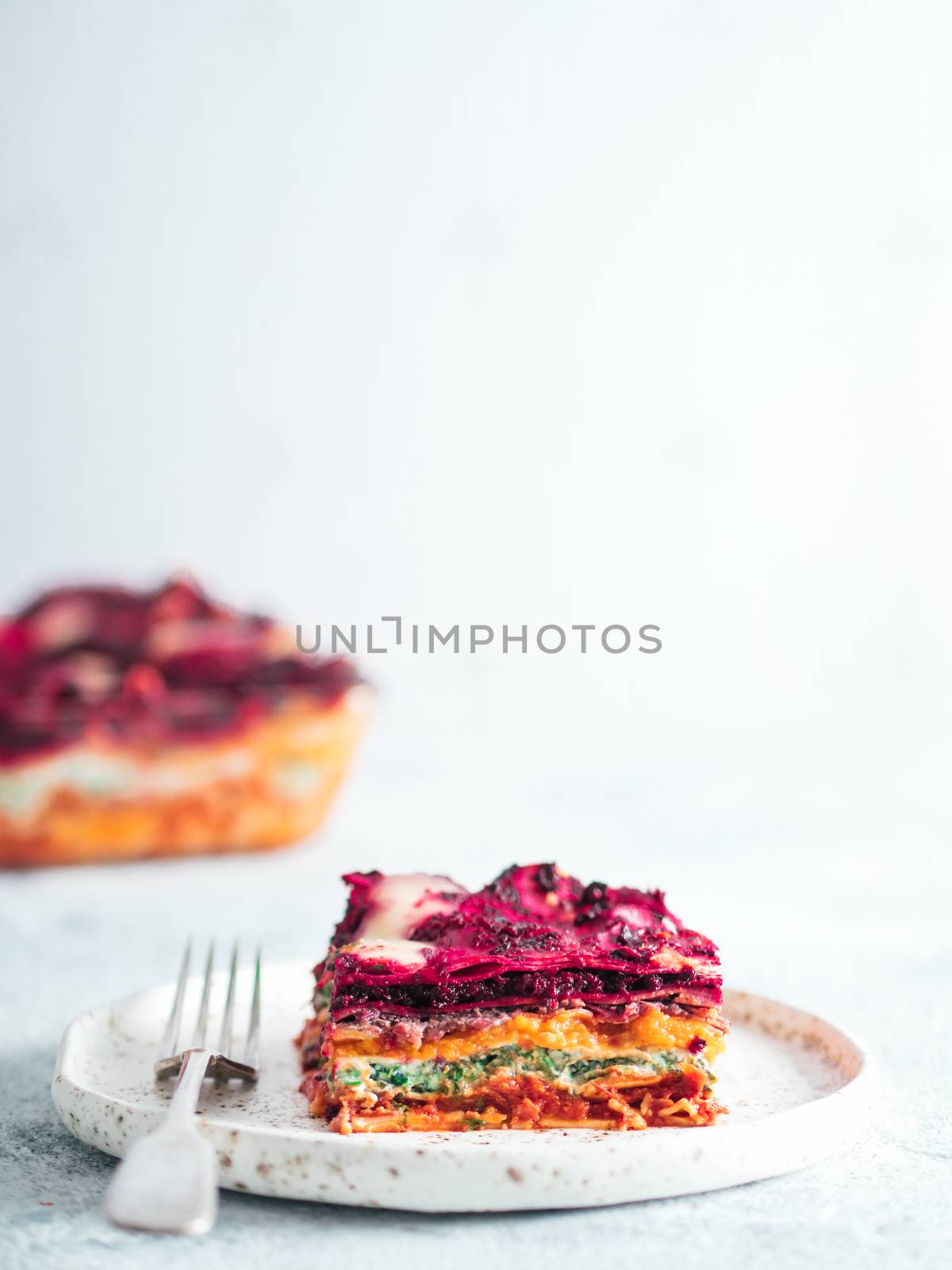 Vegetable Packed Rainbow Lasagne on craft plate.Ideas and recipes for healthy vegetarian dinner or lunch. Lasagne with beetroot,pumpkin,mushrooms,ricotta,spinach,mozarella on white table. Copy space