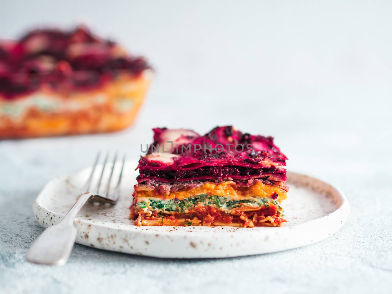 Vegetable Packed Rainbow Lasagne on craft plate.Ideas and recipes for healthy vegetarian dinner or lunch. Lasagne with beetroot,pumpkin,mushrooms,ricotta,spinach,mozarella on white table. Copy space