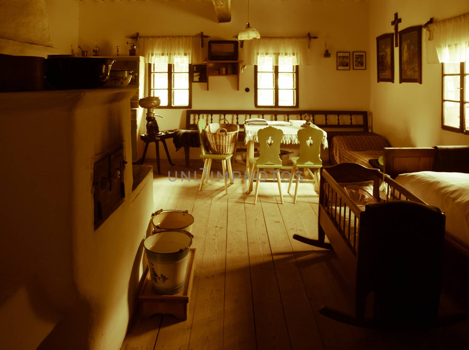 Vintage room with bed, cradle, furnace, table and chairs in old rural house. Sepia style image.