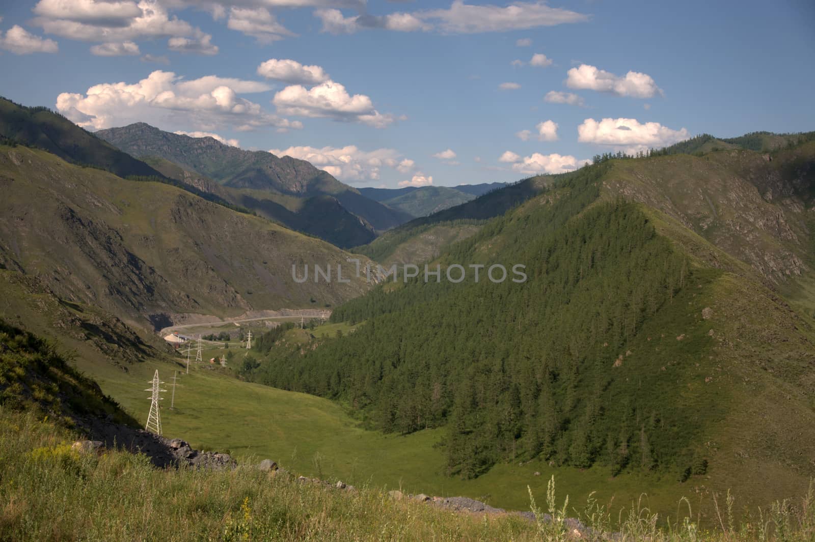 Power line posts go through a mountain valley. Altai, Siberia, Russia.