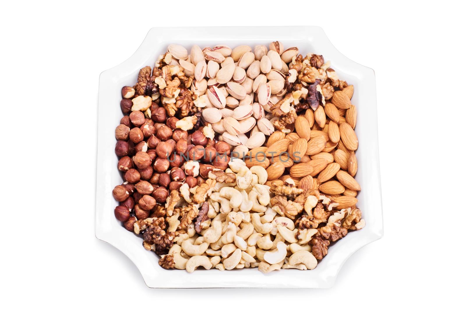 Top view of a mixture of almonds, hazelnuts, walnuts, cashews and pistachios on a ceramic plate, isolated on white background.