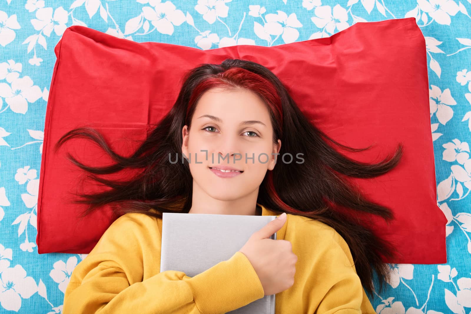 A portrait shot of a beautiful young girl lying in her bed and holding a book.
