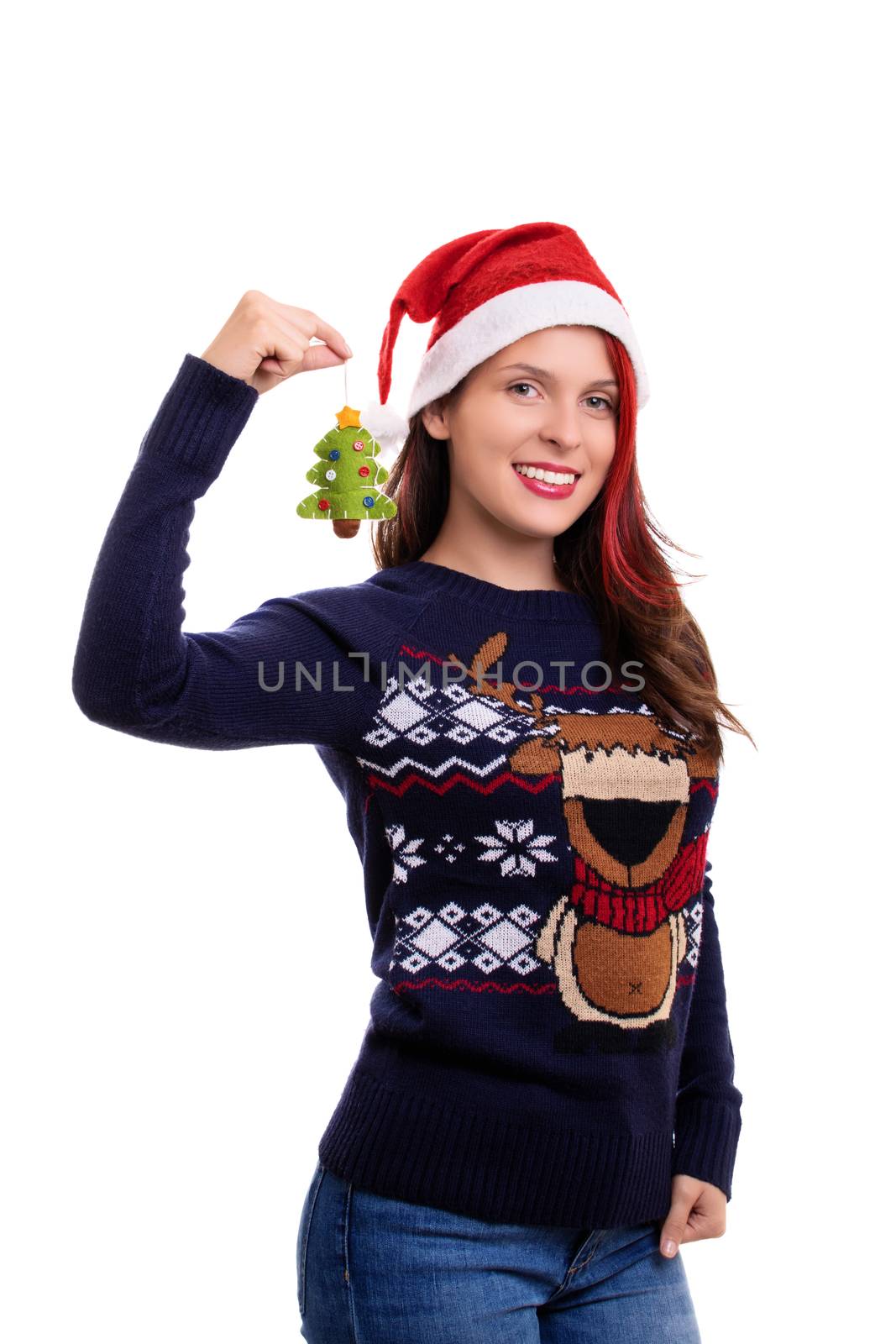 Beautiful smiling girl in a festive sweater with a Santa's hat on, holding a Christmas tree decoration, isolated on a white background.