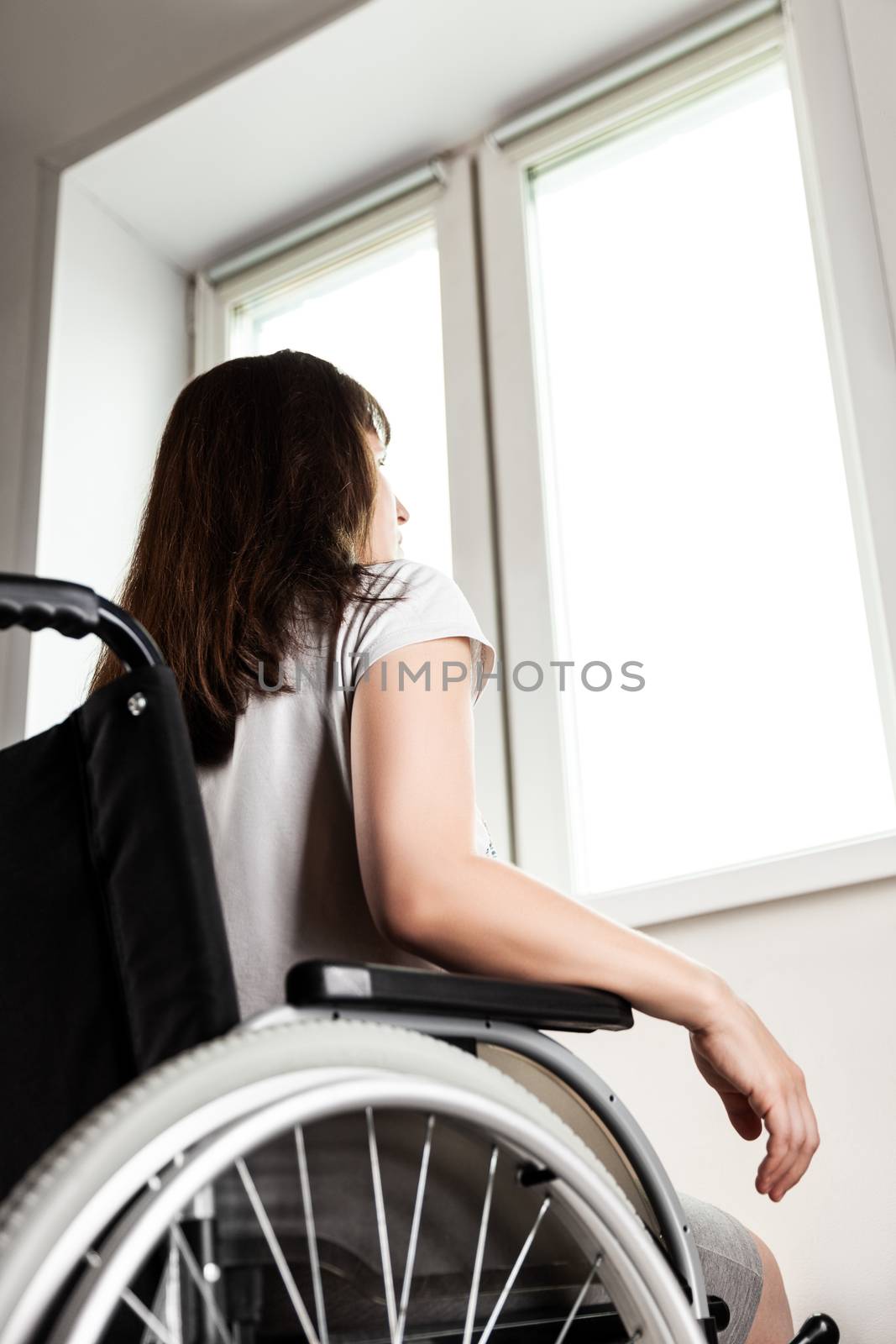 Invalid or disabled woman sitting wheelchair looking window daylight by ia_64