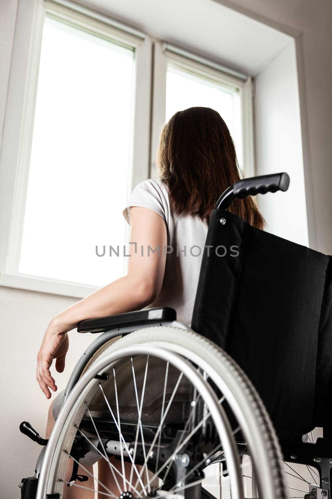 Invalid or disabled woman sitting wheelchair looking window daylight by ia_64