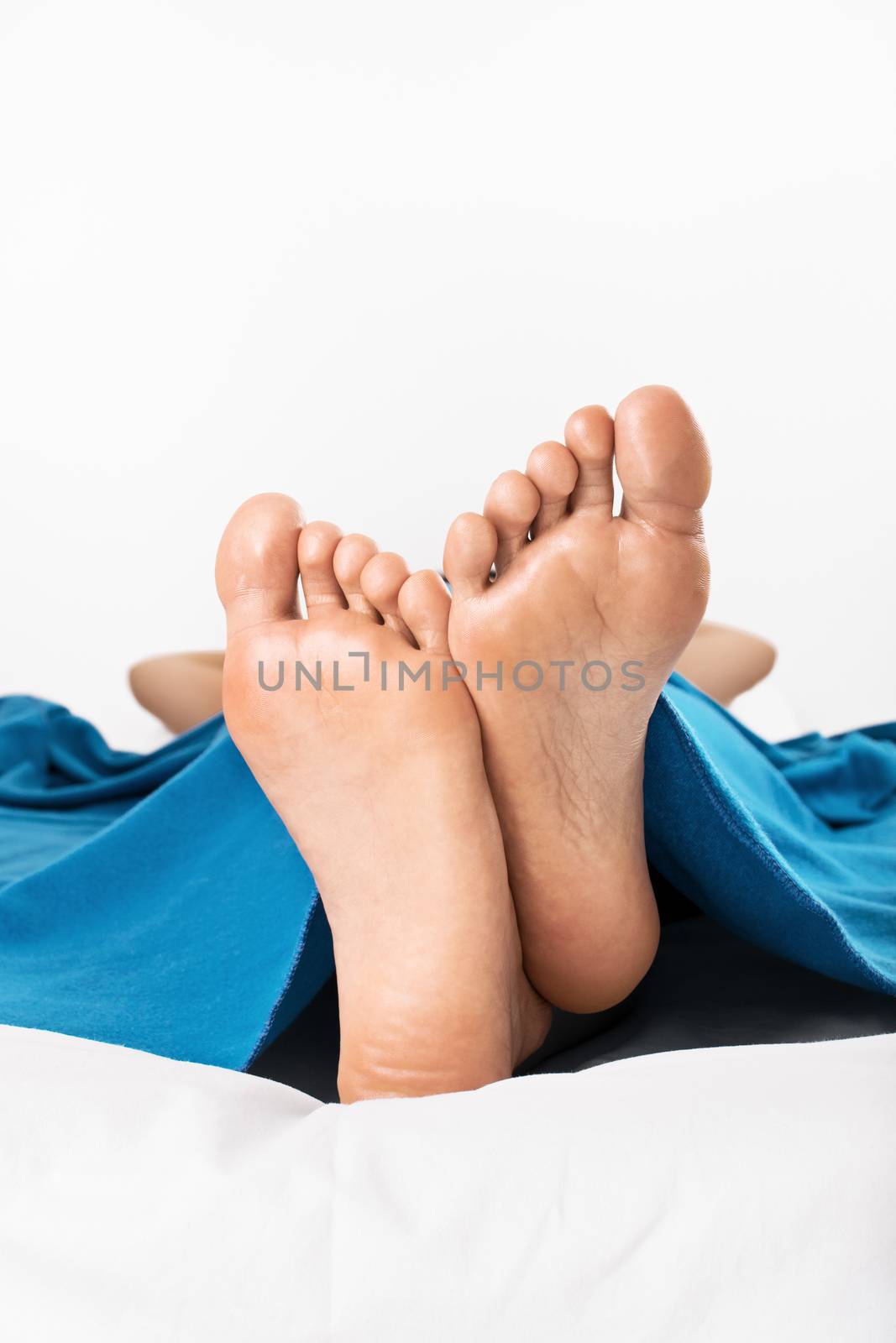 Close-up shot of female feet under the blanket, isolated on white background.