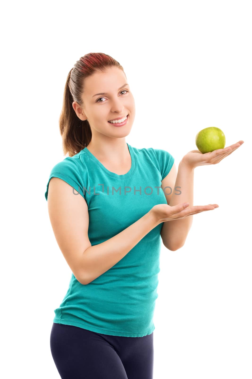 Have a bite? It's fresh and healthy. Smiling beautiful fit girl in fitness clothes holding and offering a green apple, isolated on white background.