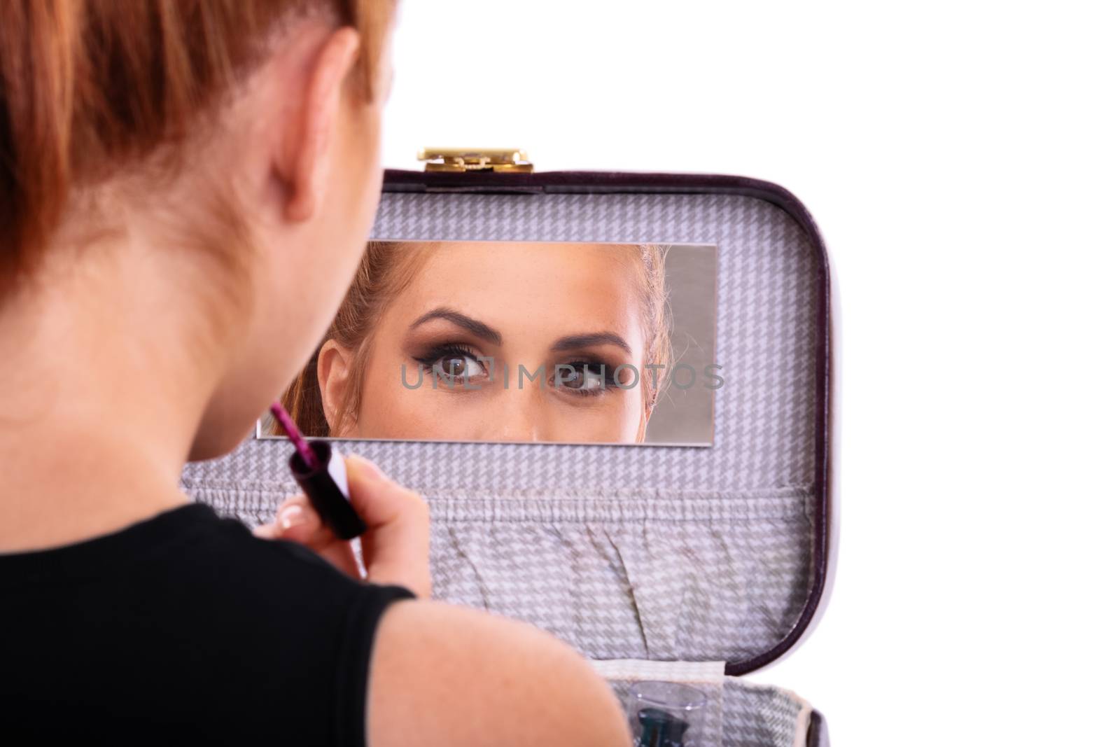 A portrait of a beautiful young girl fixing her makeup and looking in the mirror, isolated on white background.