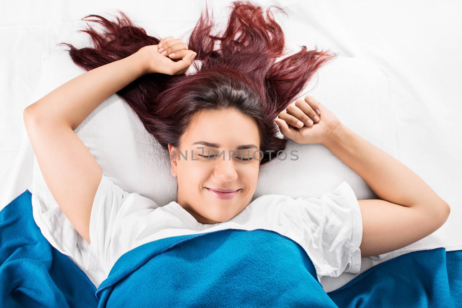 Close up of a beautiful smiling young girl waking up fresh and stretching in bed, isolated on white background.