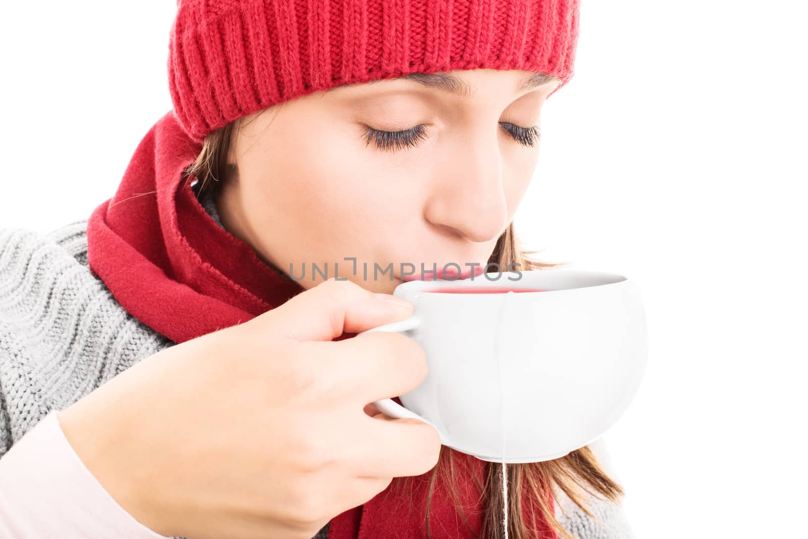 Close-up shot of a young girl wearing winter clothes and drinking a cup of hot drink, isolated on white background.
