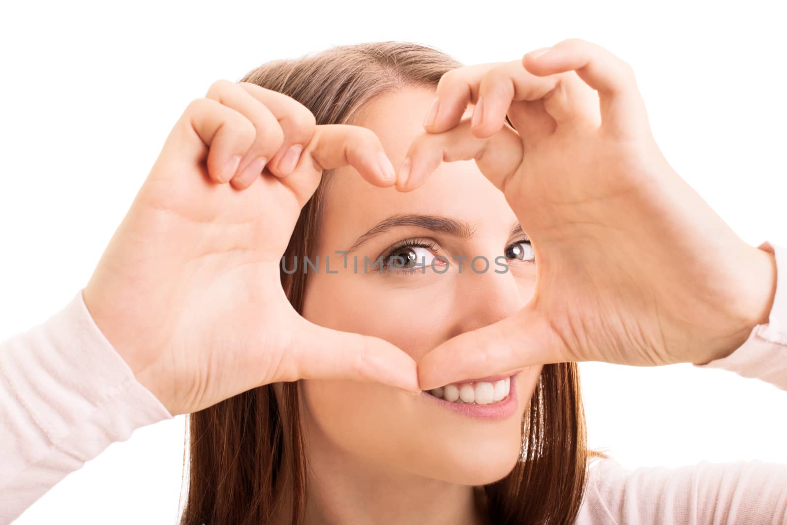 Close up beauty portrait of a smiling young girl looking through a heart shaped hands, isolated on white background.