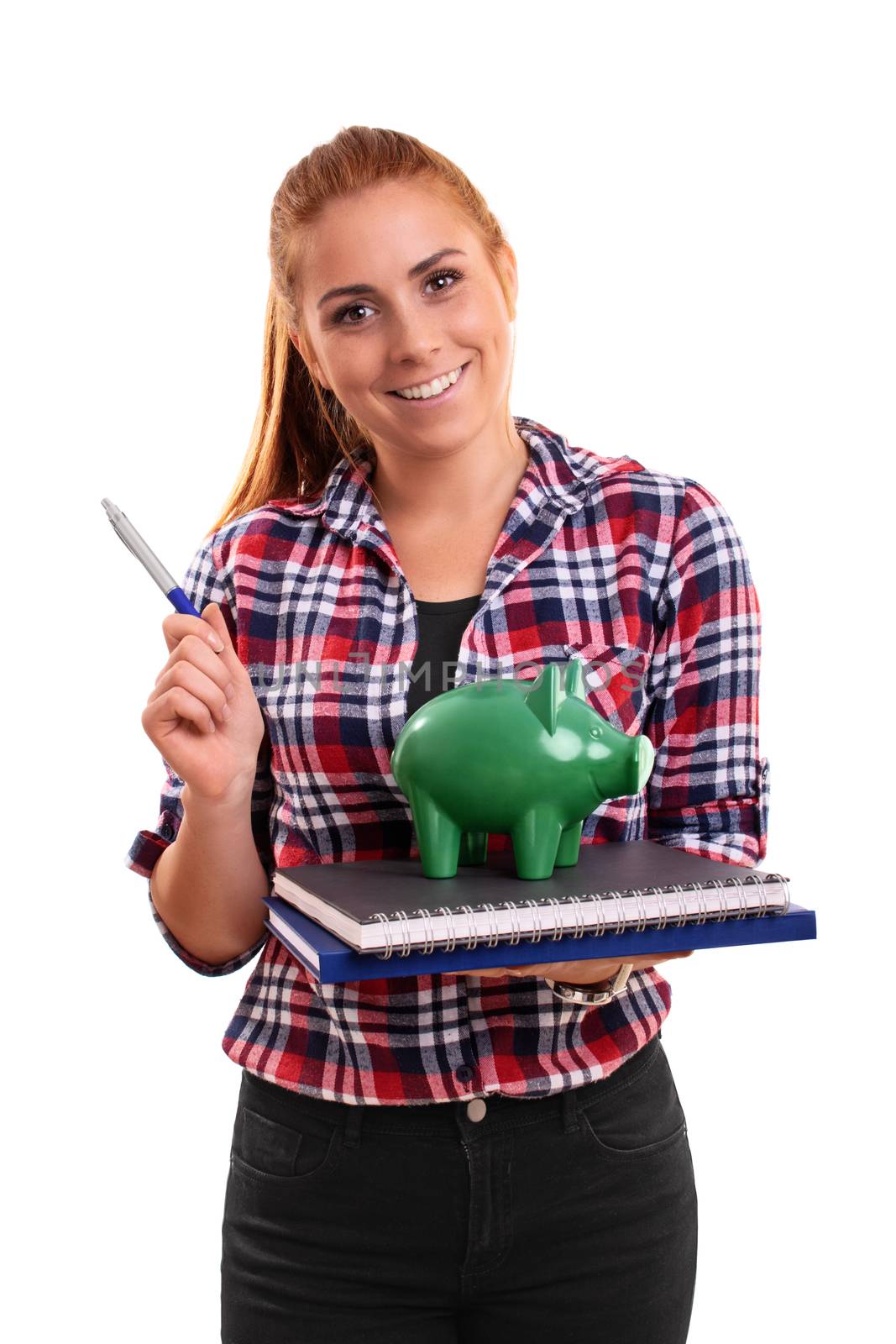 Smiling young student holding a green piggy bank on a stack of books, pointing with a pen, isolated on white background.