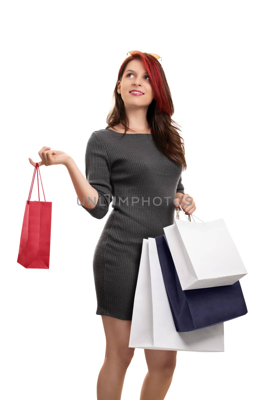 Girl in a shopping spree. A portrait of an excited beautiful young girl in a dress, holding a lot of shopping bags, isolated on white background. Girl thinking what to buy next.