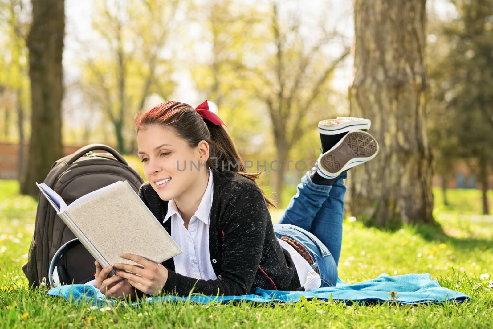 Student lying on a meadow reading a book by Mendelex