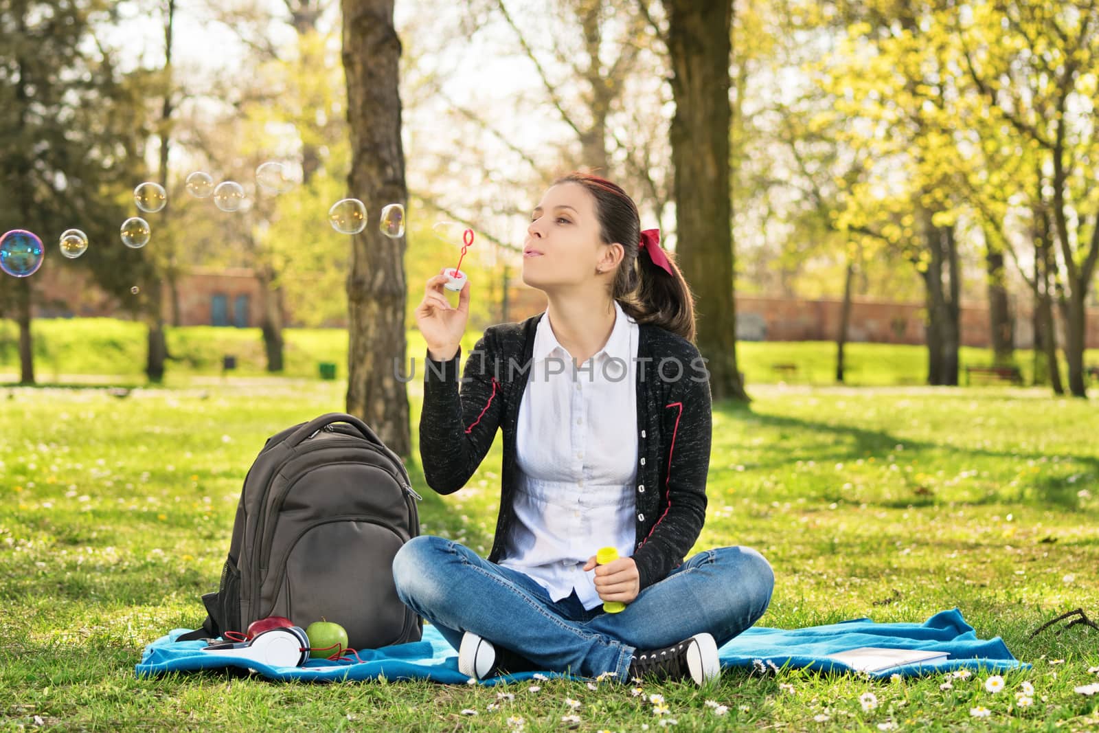 Student sitting on a meadow blowing soap bubbles by Mendelex