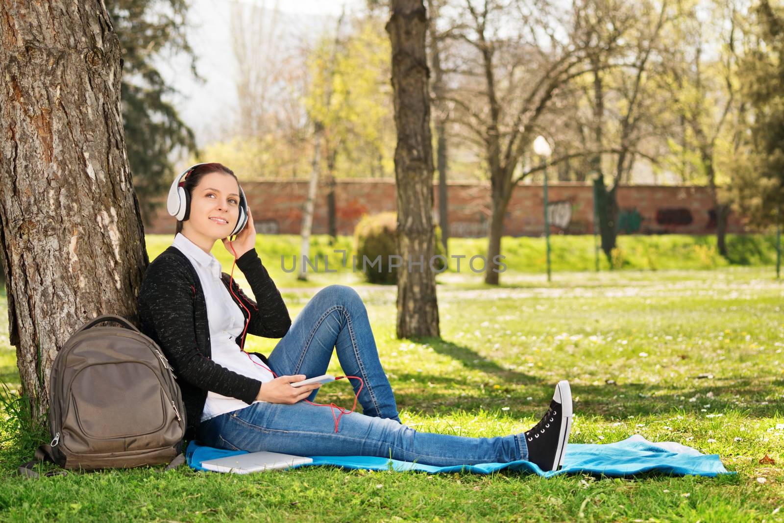 Enjoying nature while listening to music. Beautiful young student sitting on grass in a park, listening to music, making a break from her studying.
