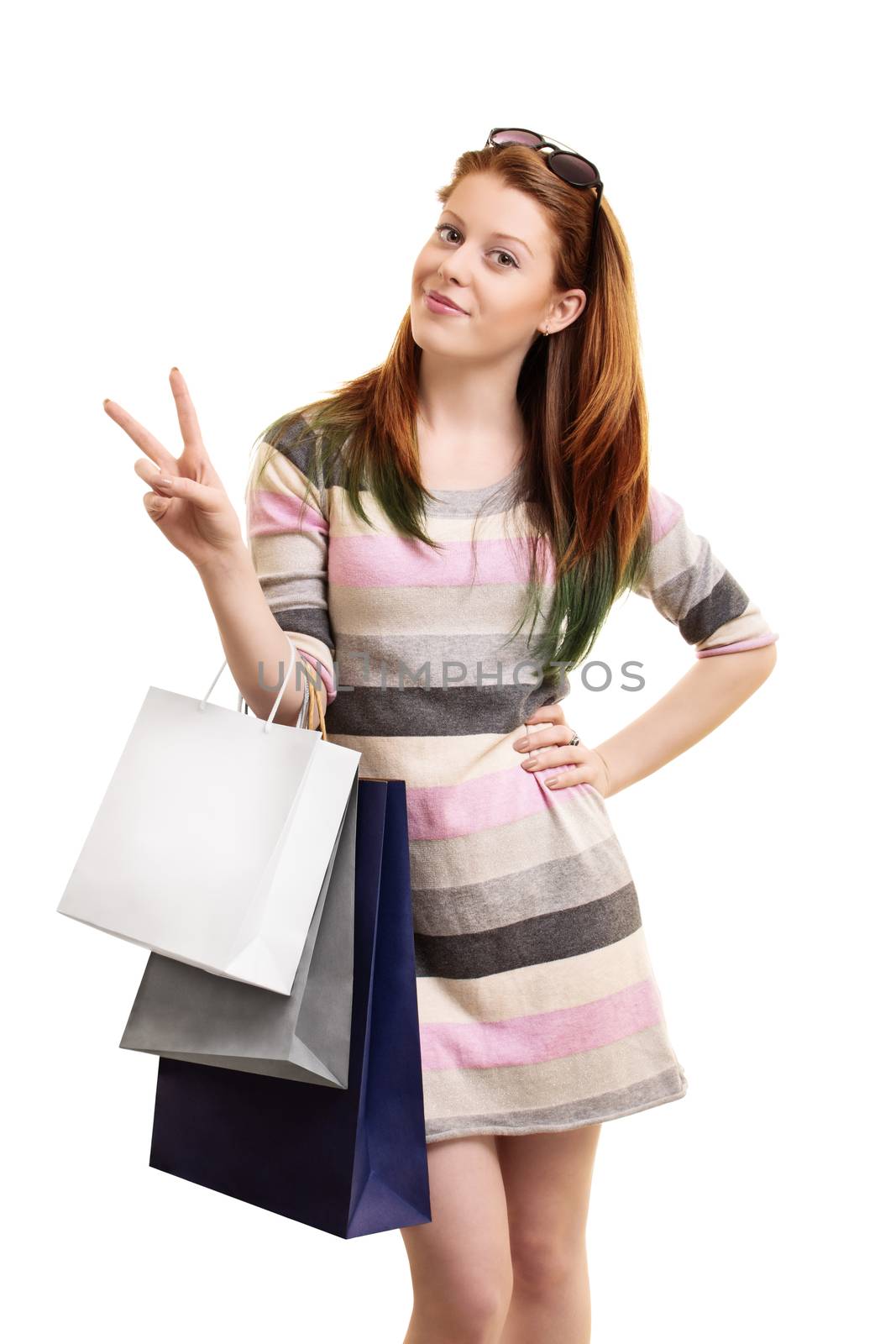 Beautiful young girl holding shopping bags and making a peace sign, isolated on a white background.