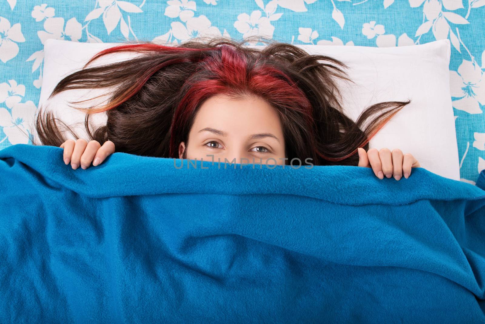 Young girl hiding behind a blanket on her bed by Mendelex