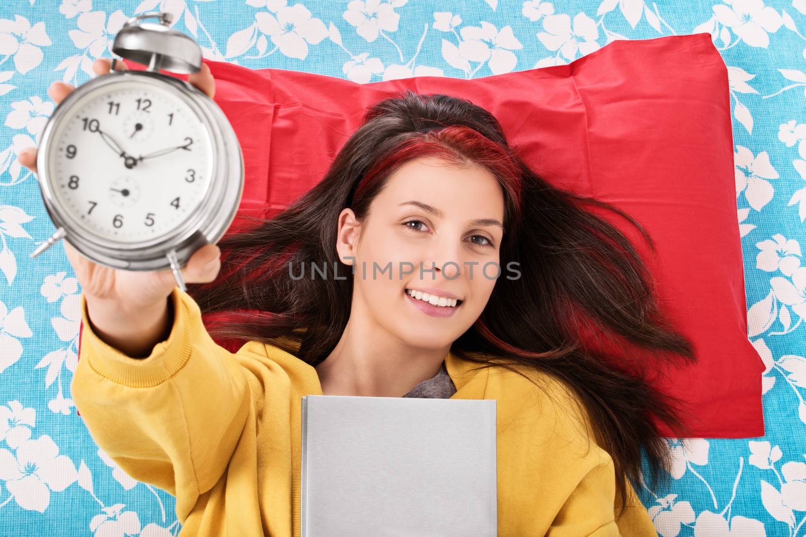 Done my reading right on time. Young girl lying in bed, holding a book and alarm clock. I'm done with my studying.