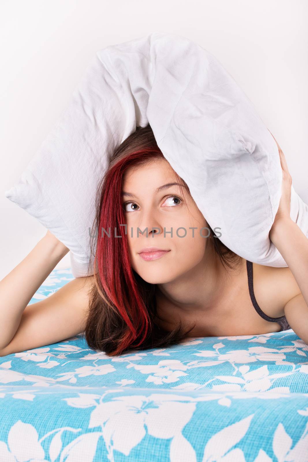 Enough with the noise! Young girl in bed holding a pillow on top of her head, covering her ears.